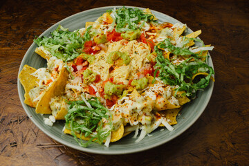 Overhead Shot of Traditional Mexican Chilaquiles with Ground Beef, Guacamole, Lettuce, Tomato and Cheese on a Rustic Wooden Table