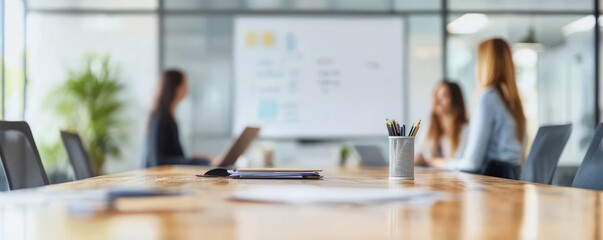 Modern office meeting room with blurred people in discussion around table, pencils in holder and papers on wooden desk, bright natural light