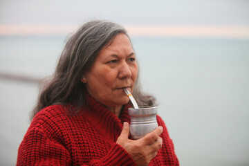 Close-up portrait of an elderly Latina woman with Guaraní features, wearing warm knitted clothes...