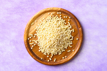 Yellow millet grain on wooden plate with purple background, Food ingredient, Top view