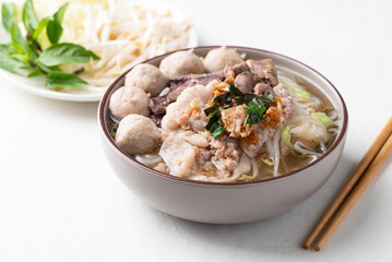 Thai noodles soup with sliced pork, minced pork, meatball and liver in a bowl eating with fresh vegetables on white background, Traditional Thai street food