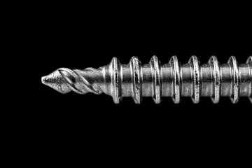 Close-up of a metallic screw with sharp threads and a pointed tip against a black background, highlighting its texture and detail