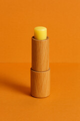 Naklejka premium A mockup of a yellow lip balm in a wooden container centered on a bright orange background showcasing natural beauty and care
