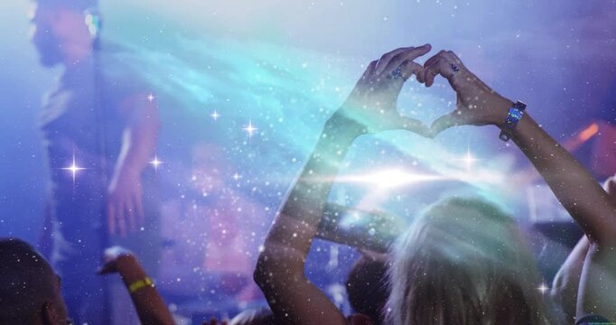 Woman lifting smartphone forming heart gesture at music show with nebula lights celebrating fandom