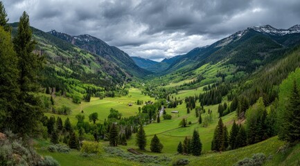 Fototapeta premium Panoramic view of a verdant valley nestled between majestic mountains under a dramatic, cloudy sky. Scattered farms and trees dot the landscape