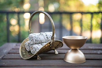 Jasmine incense burns next to a bundle of sage on an outdoor table ready for a cleansing and...