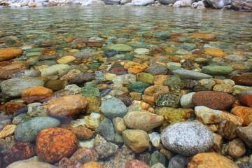 Fototapeta premium Colorful pebbles submerged in clear water at a serene riverbank with smooth stones