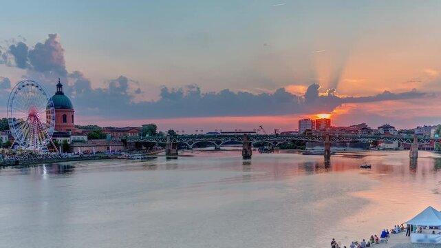 Aerial view of La Grave Hospital with Saint-Pierre Bridge. Port de la Daurade park along the Garonne River timelapse in Toulouse, France. Sunset colorful clouds, ferry at dock and riverside atmosphere