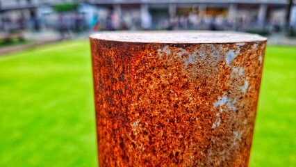 A rusted iron pole with green grass in the background. The texture of the rust on the iron peeling...