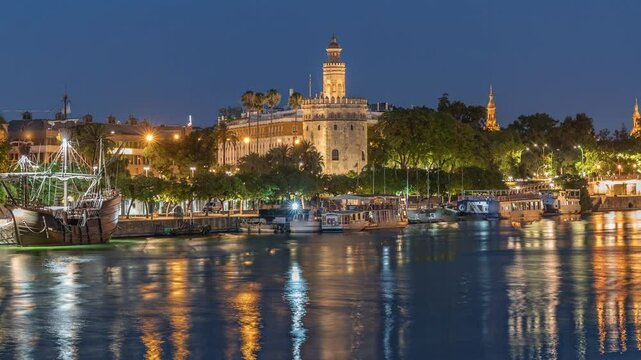 Torre del Oro watchtower in Seville, Spain. Day to night transition timelapse with city lights reflecting on water and scenic aerial view of waterfront. Tour boat floating along the Guadalquivir River