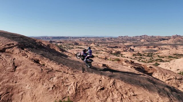 Dirt biker performs wheelie over sandstone ridge above vast Utah canyonlands