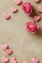 Flatlay of pink hearts and roses on textured beige paper, leaving a central blank space ideal for text or message