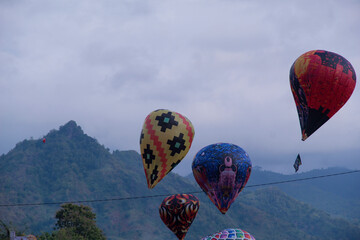 Traditional hot air balloons rise against a scenic mountain backdrop during a cultural festival in...