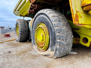 Close up of flat tyre of large old quarry dump truck. Big green rusty mining truck out of work standing for exhibition on the coast of Peru in San Juan de Marcona. Mining truck