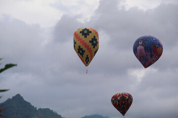 Traditional hot air balloons rise against a scenic mountain backdrop during a cultural festival in...