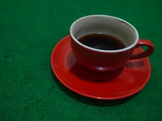 A vibrant red coffee cup and saucer on a textured green background.