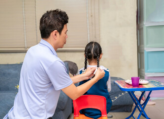 Father does his little daughter's hair in the living room in the morning before she goes to school.