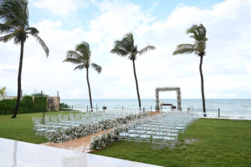 Fototapeta premium outdoor wedding ceremony altar overlooking the sea, surrounded by palm trees and with a central path towards the ocean, beachfront wedding altar with palm trees, seaside ceremony, destination weeding