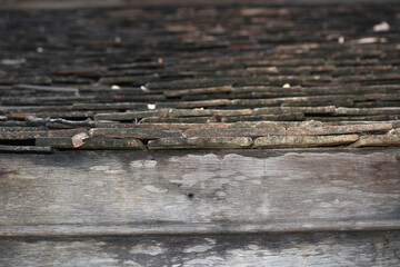Rows of weathered, moss-covered terracotta roof tiles are stacked above a decaying wooden beam,...