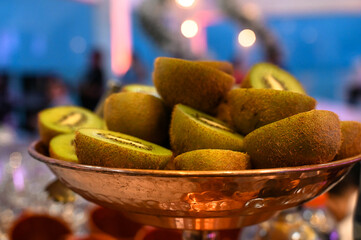 fresh sliced kiwis served in copper bowl at event, tropical fruit display on cocktail bar counter,...