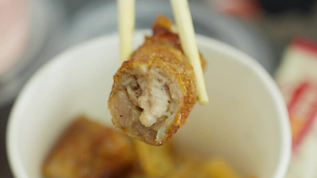 A crispy Fujian-style five-spice meat roll is lifted with chopsticks&mdash;showing golden exterior and flavorful filling, capturing tactile texture and the savory essence of traditional Southern Chinese sna