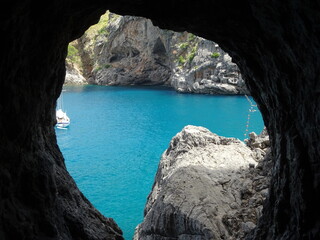 Hidden sea view from cave with sailboat and turquoise water Mallorca