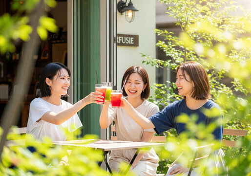 Three Happy Asian Friends Toasting with Refreshing Drinks at a Sunny Outdoor Cafe