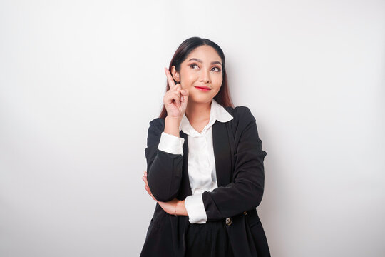 Excited Asian businesswoman wearing black suit pointing at the copy space on top of her, isolated by white background