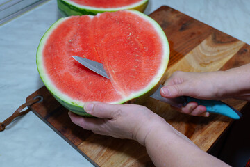 Hands using knife to cut fresh watermelon on wooden cutting board, preparing delicious summer snack