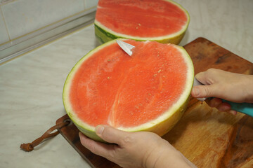 Hands cutting a fresh, juicy watermelon on a wooden cutting board, preparing a refreshing summer treat
