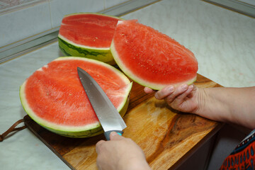 Hands cutting fresh watermelon on wooden cutting board, preparing refreshing summer treat