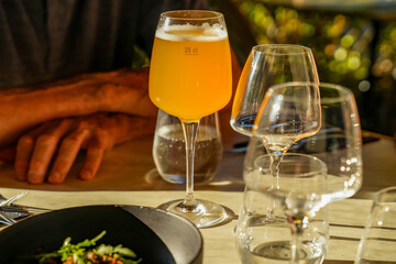 Restaurant table set outdoors. A glass of beer illuminated by the sun. Hands of a man sitting at...