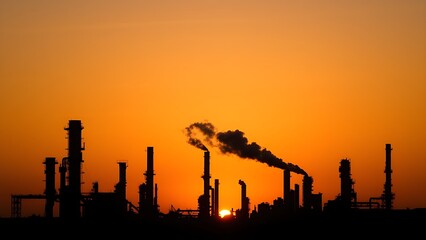 Obraz premium Industrial refinery silhouette at sunset with steam plumes against a dramatic gradient sky.