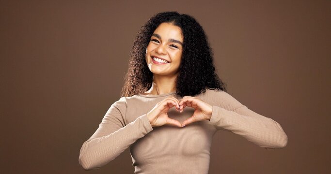 Heart hands, smile and portrait of woman in studio for support, kindness and thank you. Gratitude, happiness and emoji sign with person on brown background space for love gesture and care symbol