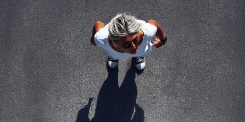 Woman stands on asphalt ground looking up, from top view