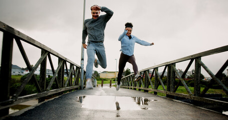 Exercise, running and couple with jumping on bridge for pace training, winter workout and teamwork. Fitness, puddle and people with cardio outdoor for race endurance, marathon competition and support