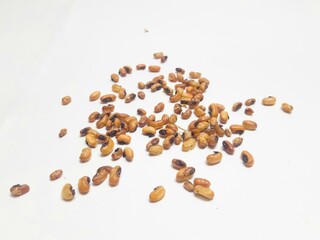A close-up of roasted soybeans scattered on a white background, showcasing their golden brown texture and crunchy appearance.