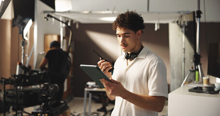 Man, filming and radio with tablet on set for discussion, reading script and shooting schedule....