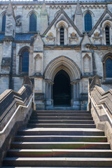 The Gothic entrance of the Cathedral of St. John the Baptist dominates the Norwich cityscape. Historic stone facade displays ornate arched doorway with ascending steps