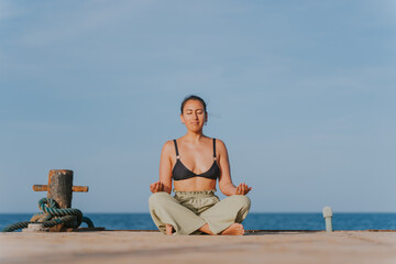 Young woman meditating on pier at sunrise, embracing serenity and ocean views