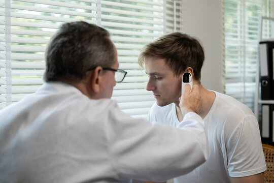 Senior doctor using ear thermometer to check patient man body temperature during a medical examination in clinic.