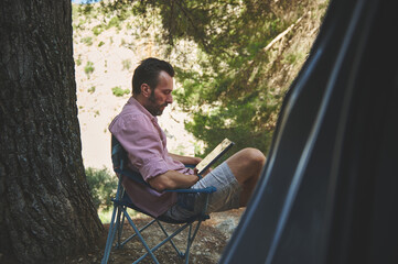 Man Relaxing in Nature While Reading a Book at a Calm Campsite