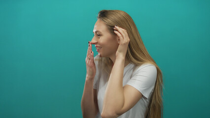 Woman listening with hand to ear wearing white shirt against blue background displaying curiosity...