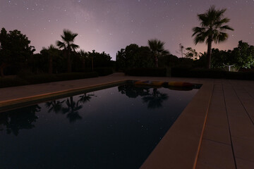 starry sky and palm trees reflect in the smooth water surface of a swimming pool in majorca