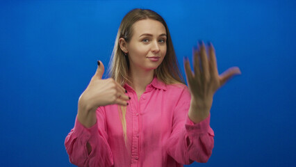 Woman gesturing confidently over an isolated blue background, wearing a bright pink shirt,...