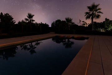 starry sky and palm trees reflect in the smooth water surface of a swimming pool in majorca