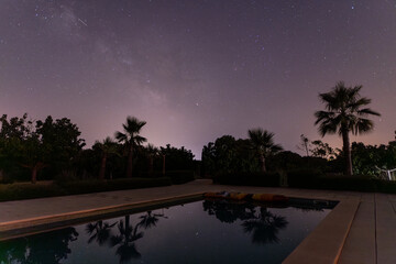 starry sky and palm trees reflect in the smooth water surface of a swimming pool in majorca
