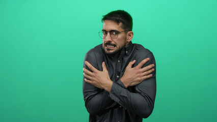 Young man shivering from cold in front of a vibrant green wall, portraying discomfort with a tense...