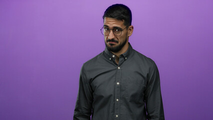 Young man with glasses standing against purple background showcasing a confident expression