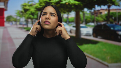 Woman holds her ears while covering at a busy street outdoors, the young latin hispanic individual...